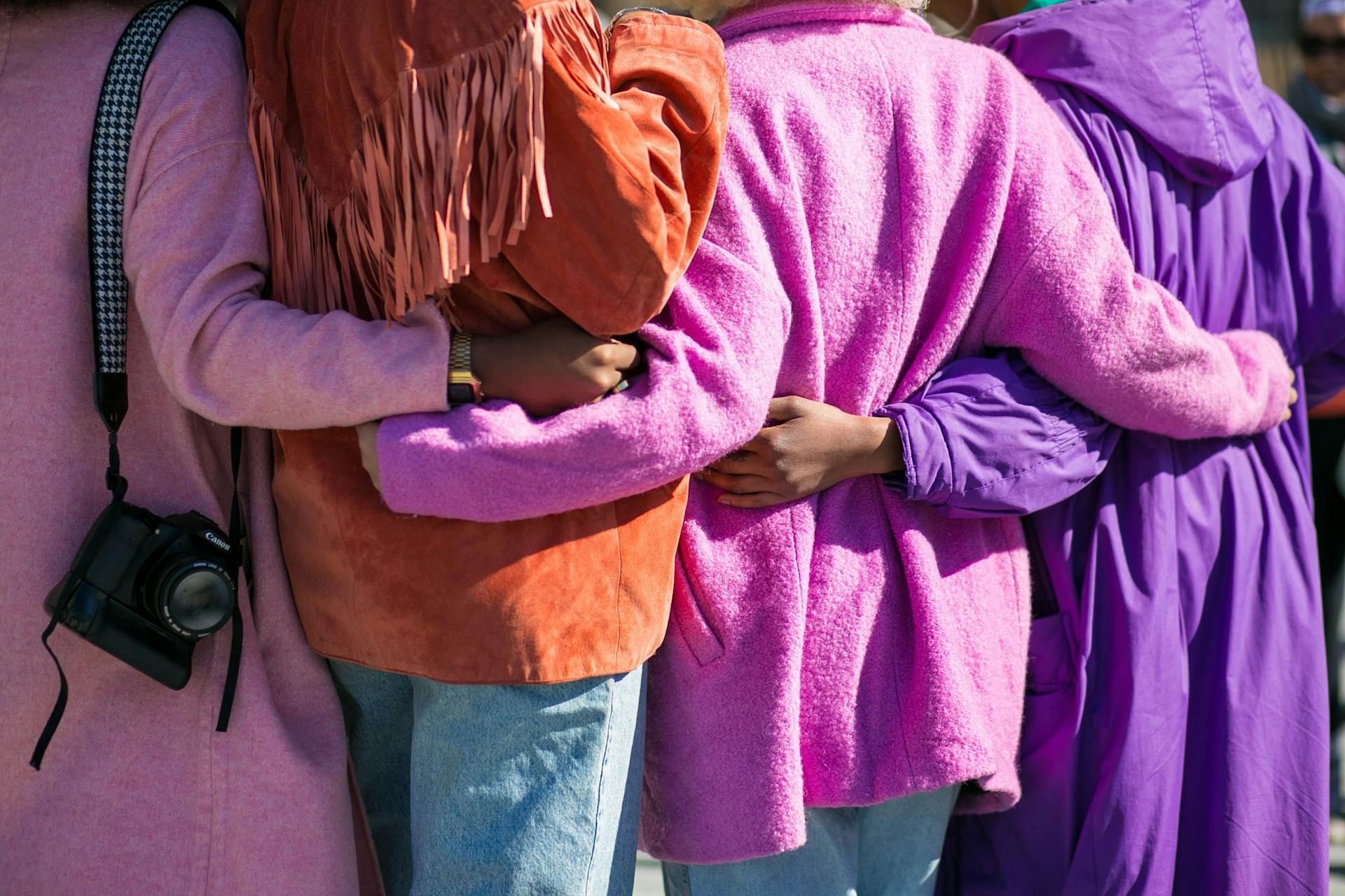 People dressed in colours are hugging and holding each other.